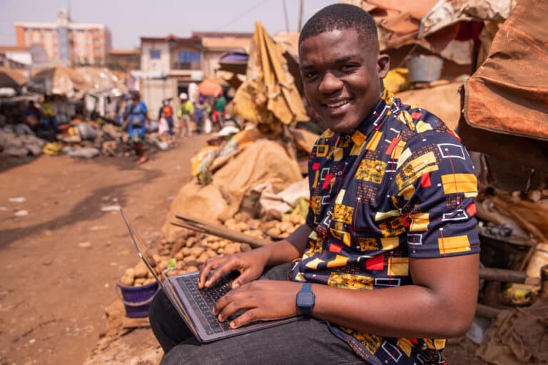 Young African man uses his computer at the market.