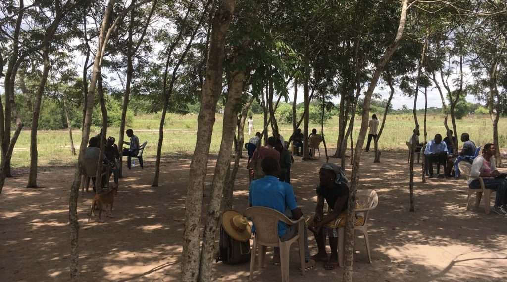 IFPRI agricultural field project with people seating in pairs under some trees during survey interviews