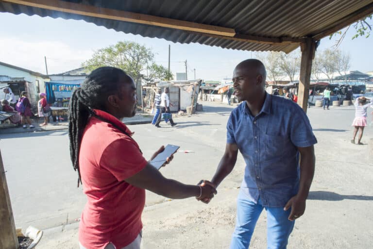 Two men shake hands in Capetown, South Africa. One man will interview the other using a mobile tool for primary data collection.