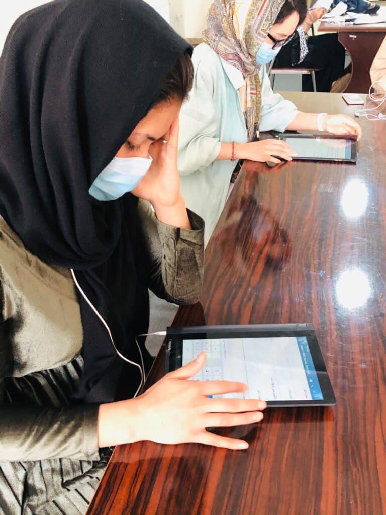 An enumerator conducting a phone interview using a tablet connected with headsets. The tablet is on a table