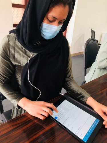 A woman in a medical mask uses SurveyCTO on a mobile device.
