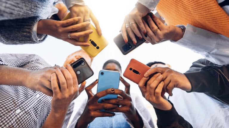 A group of people stand in a circle holding brightly colored smartphones.