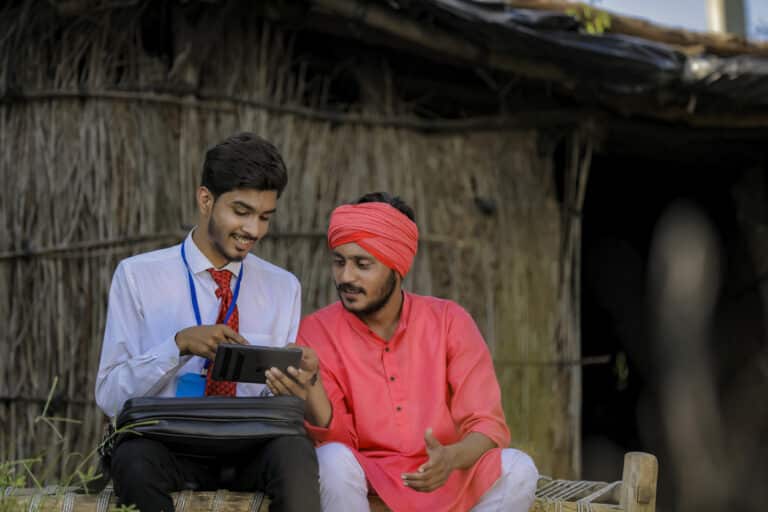 Two Indian men look at a smartphone with a mobile data collection app on it.
