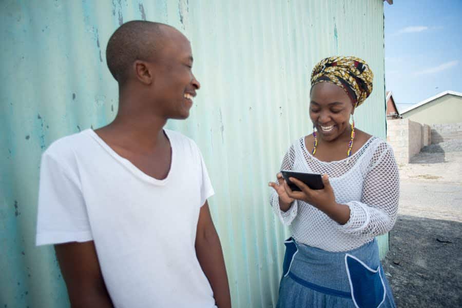 A woman interviews a man using a survey on a mobile device in South Africa.