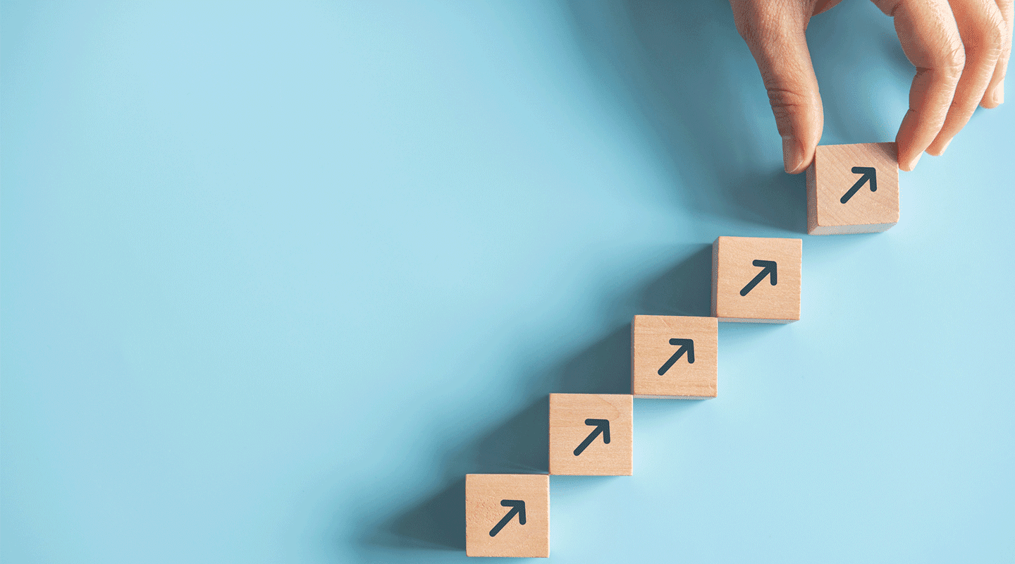 Close up man hand arranging wood block stacking as step stair on paper blue background to illustrate overcoming M&E challenges.