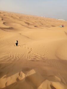 Woman climbing up a sand dune in the desert of Dubai.