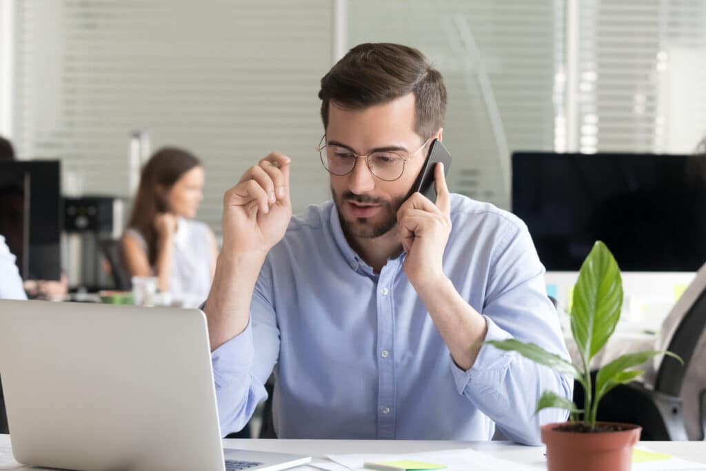 Man calls a survey respondent while sitting at a desk in front of a laptop, to conduct a phone interview.